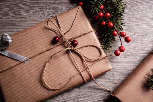 A Christmas gift wrapped in brown paper and twine with a sprig of foliage and berries
