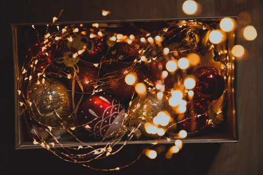 A cardboard box of old Christmas baubles in red, silver and gold, tangled with a string of fairy lights.
