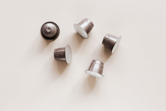 Aluminium coffee capsules scattered on a plain cream background