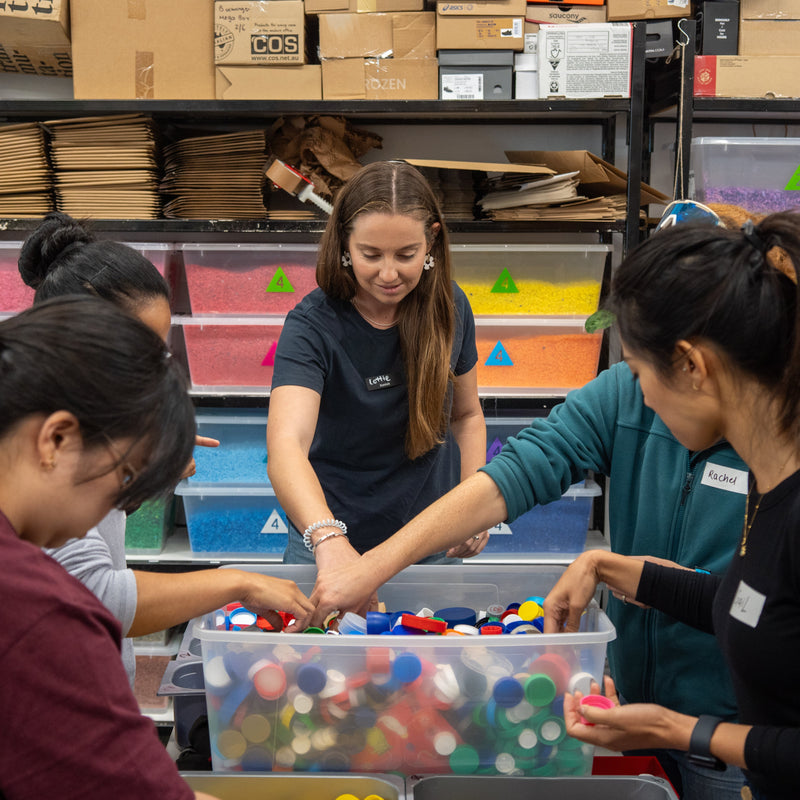 Group of people sorting colorful objects in a storage area with shelves and boxes.