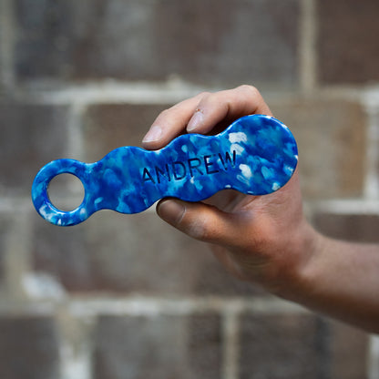 Deep Blue recycled plastic bottle opener held in a hand, engraved with the name ANDREW