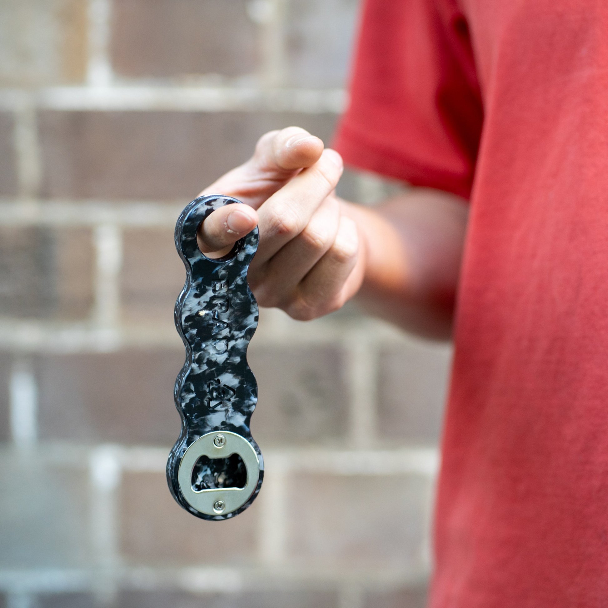 Midnight Black recycled plastic bottle opener hanging from a finger