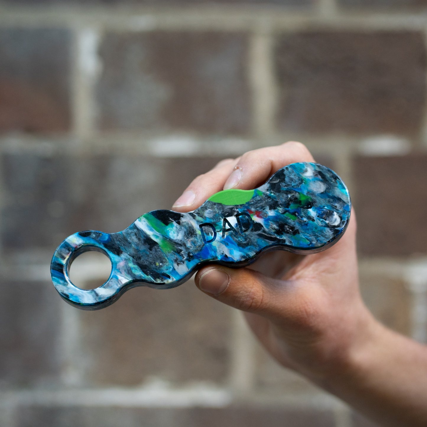 Orbital recycled plastic bottle opener held in a hand, engraved with DAD