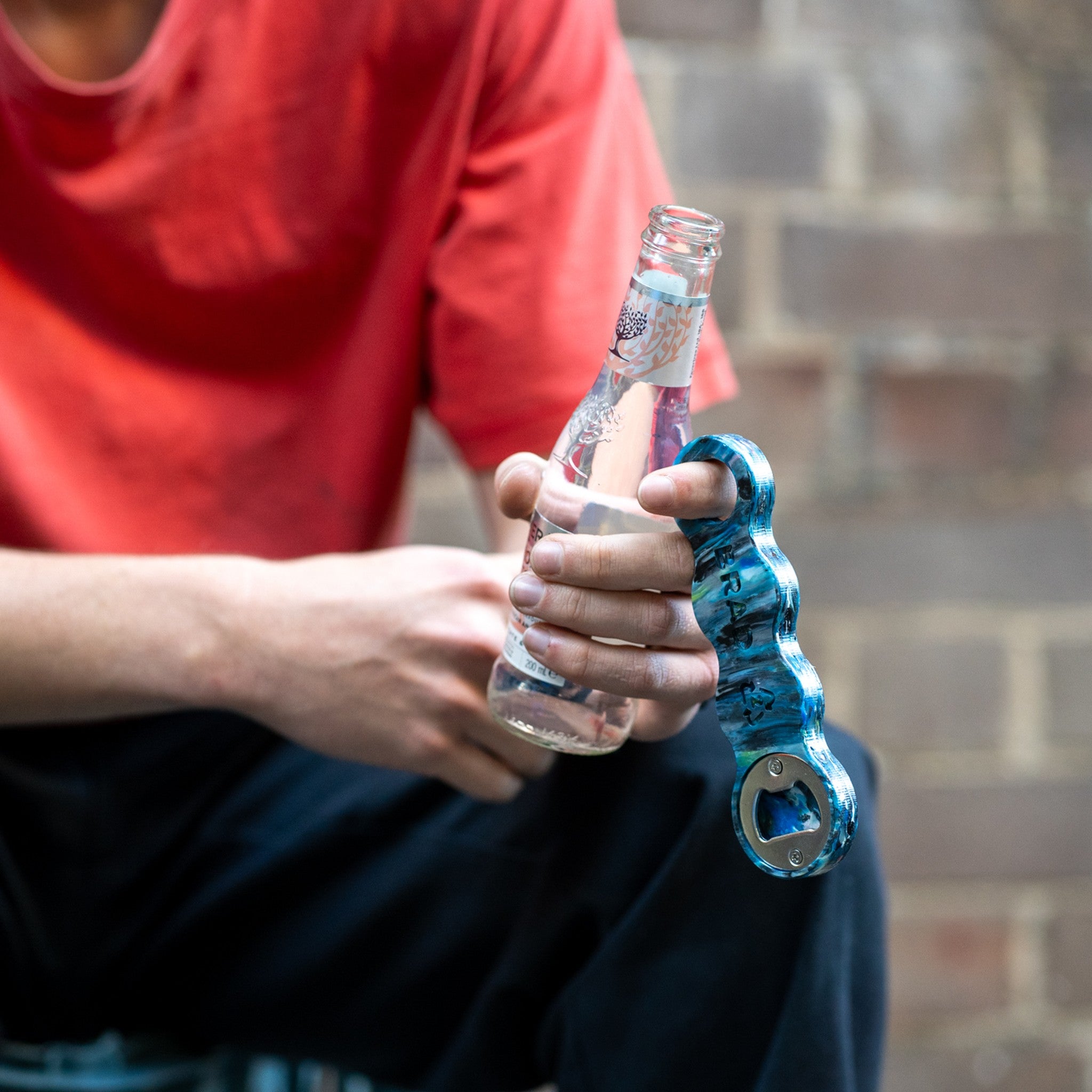 Orbital recycled bottle opener opening a bottle