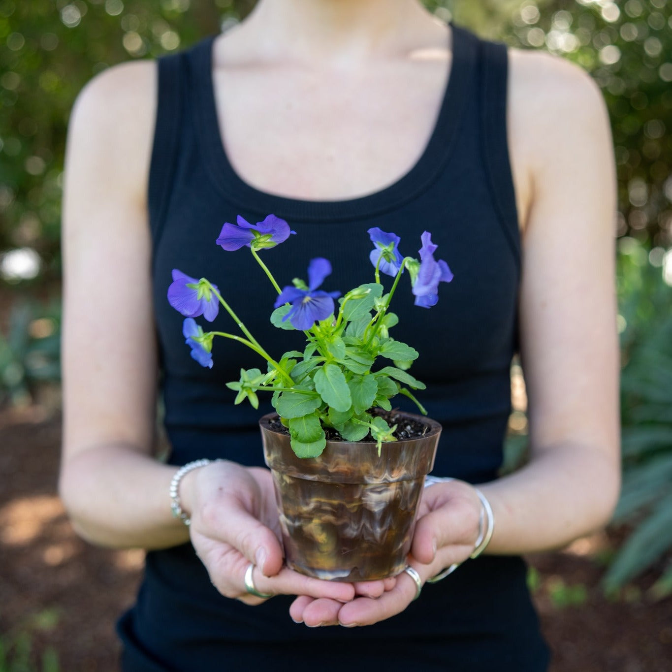 BRAD recycled plastic pot plant in Chocolate brown, eco-friendly Australian-made planter from 17 recycled milk bottle lids, held outdoors with purple flowers