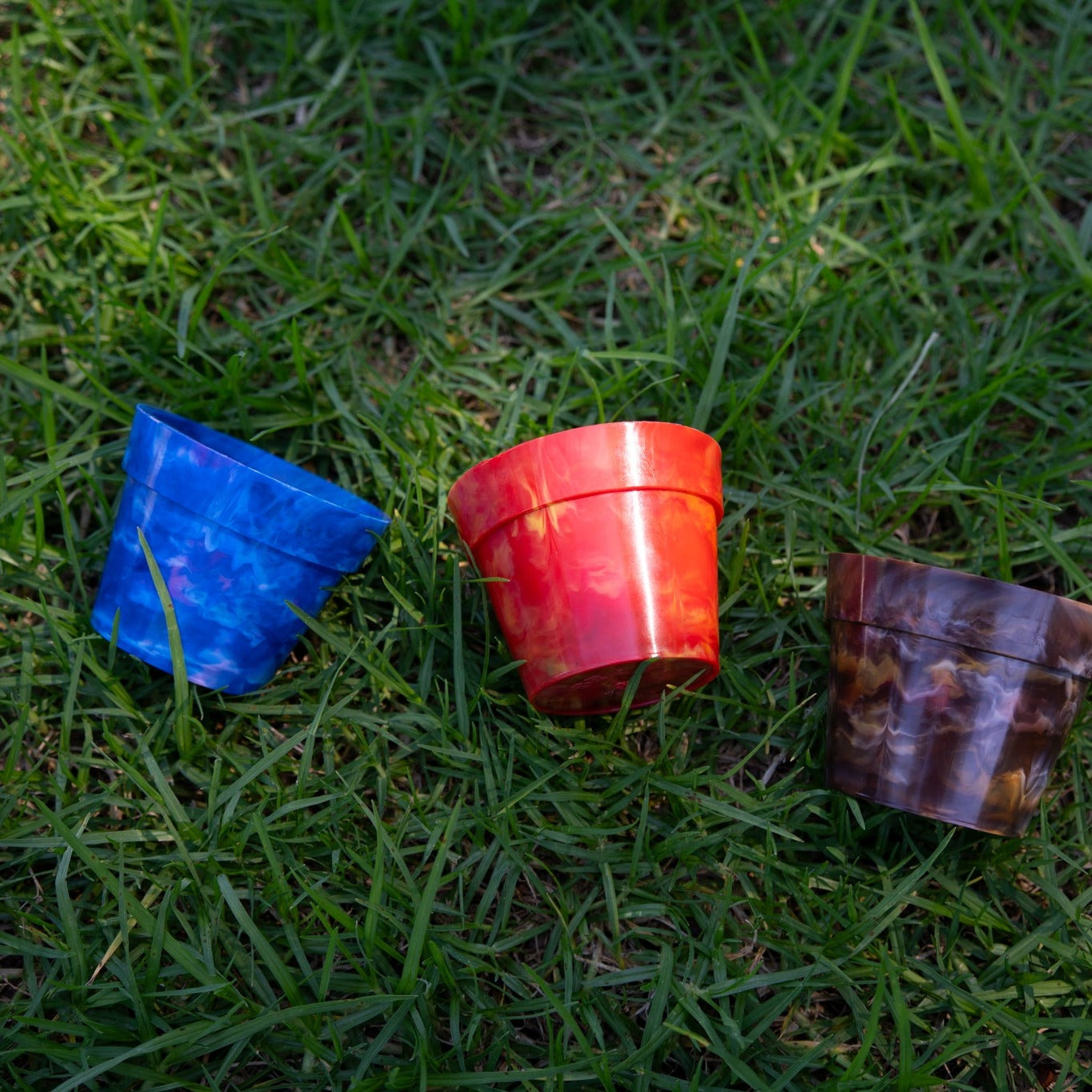 Three BRAD recycled plastic pot plants in Blueberry, Strawberry and Chocolate colours on green grass, showing the colour range of sustainable planters made from recycled milk bottle lids