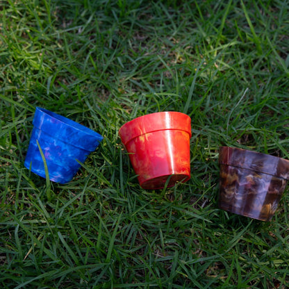 Three BRAD recycled plastic pot plants in Blueberry, Strawberry and Chocolate colours on green grass, showing the colour range of sustainable planters made from recycled milk bottle lids